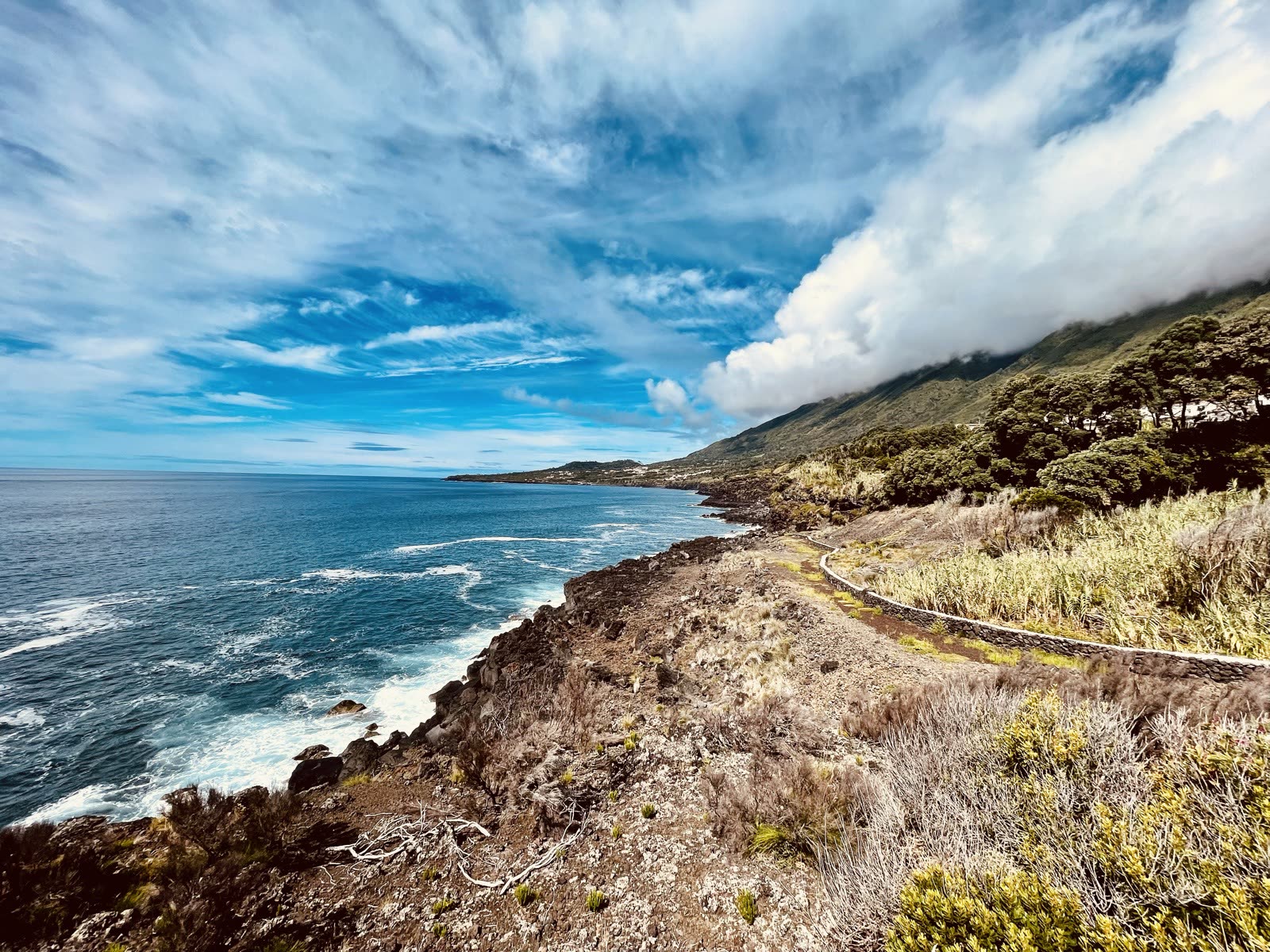 The volcanic coast of Pico Island with the Atlantic and cloud-capped slopes
